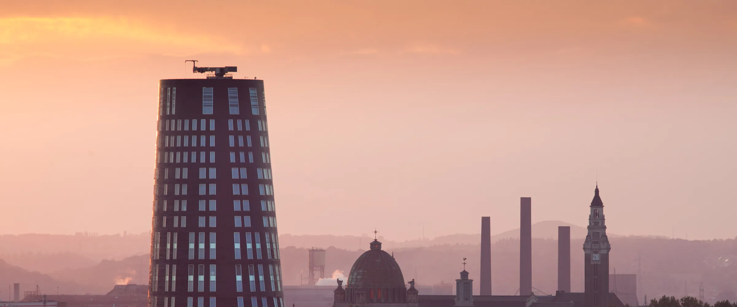 Charleroi au coucher du soleil : la Tour bleue, le dôme, le beffroi et un terril à l’horizon